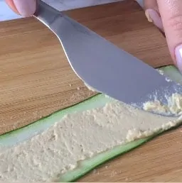 A knife spreading hummus on a zucchini