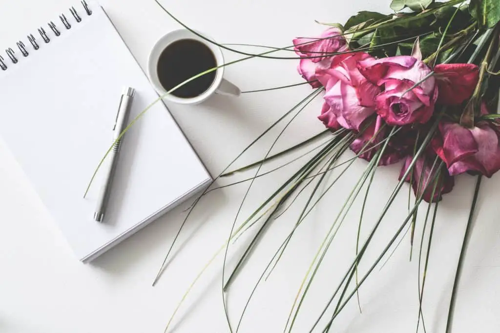 A notebook, a coffee cup and roses photographed from the top