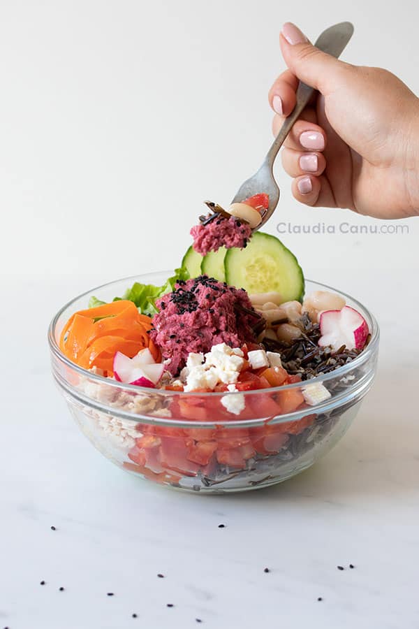 Un bol con muchos ingredientes de varios colores y una mano con un tenedor