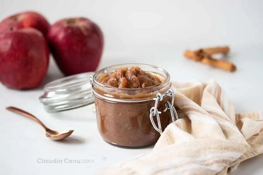 Un tarro de vidrio con compota de manzana y manzanas rojas en el fondo