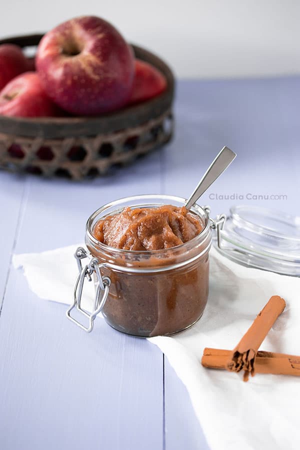 A glass jar with applesauce and apples and cinnamon stick as background