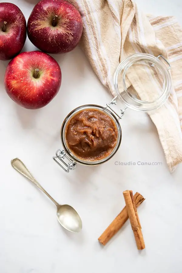 A glass jar with applesauce and apples and cinnamon stick as background