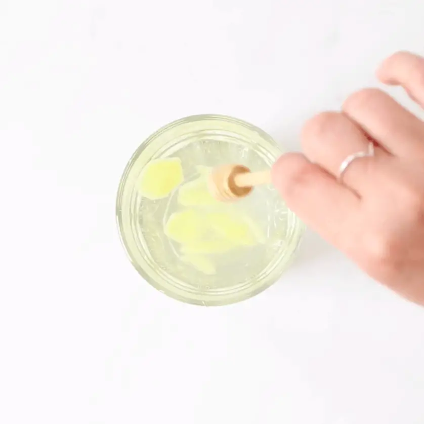 A hand adding honey to a glass with ginger water