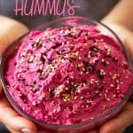 Two hands holding beetroot hummus